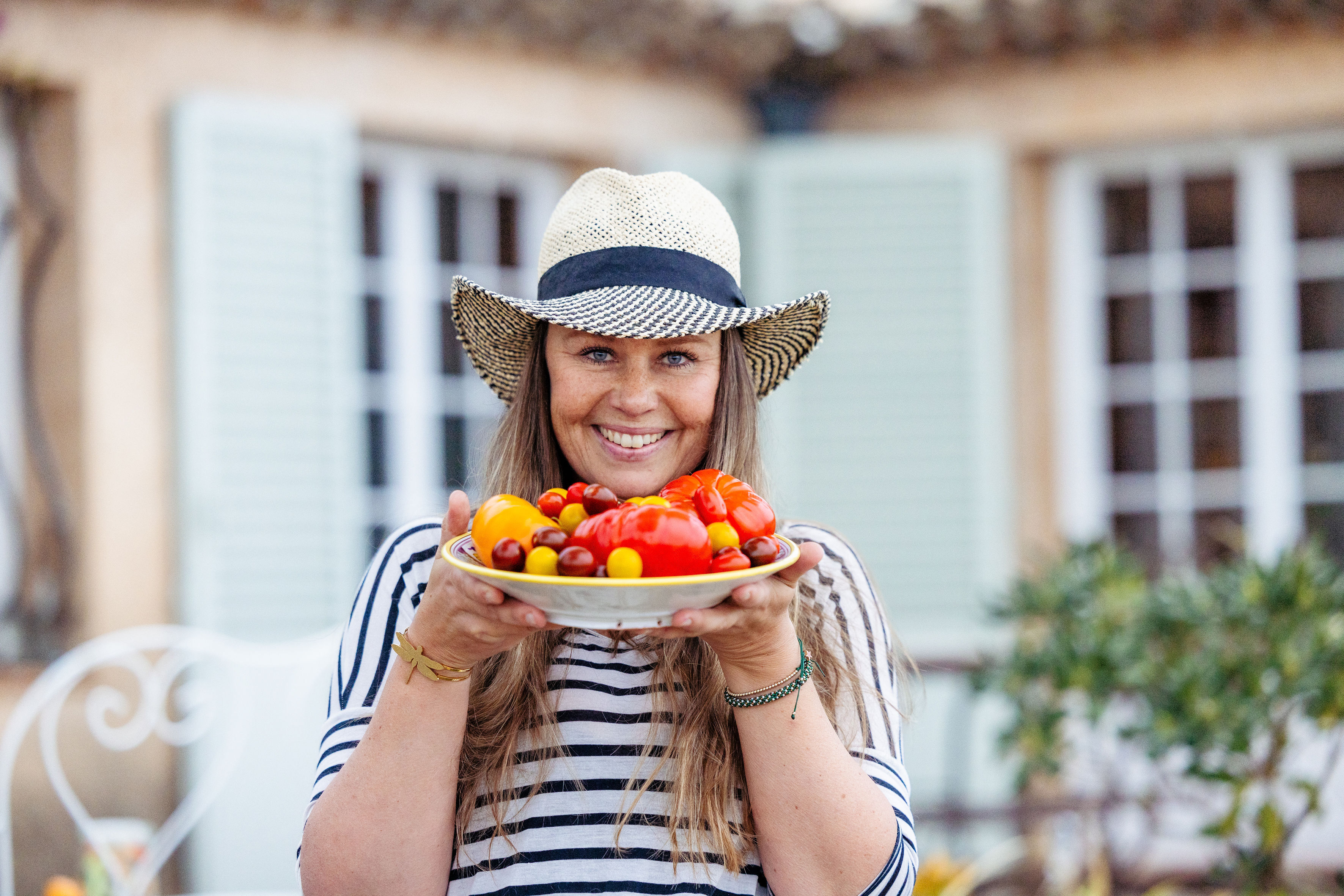 Eva holder en tallerken med fargerike tomater utenfor et provencalsk hus