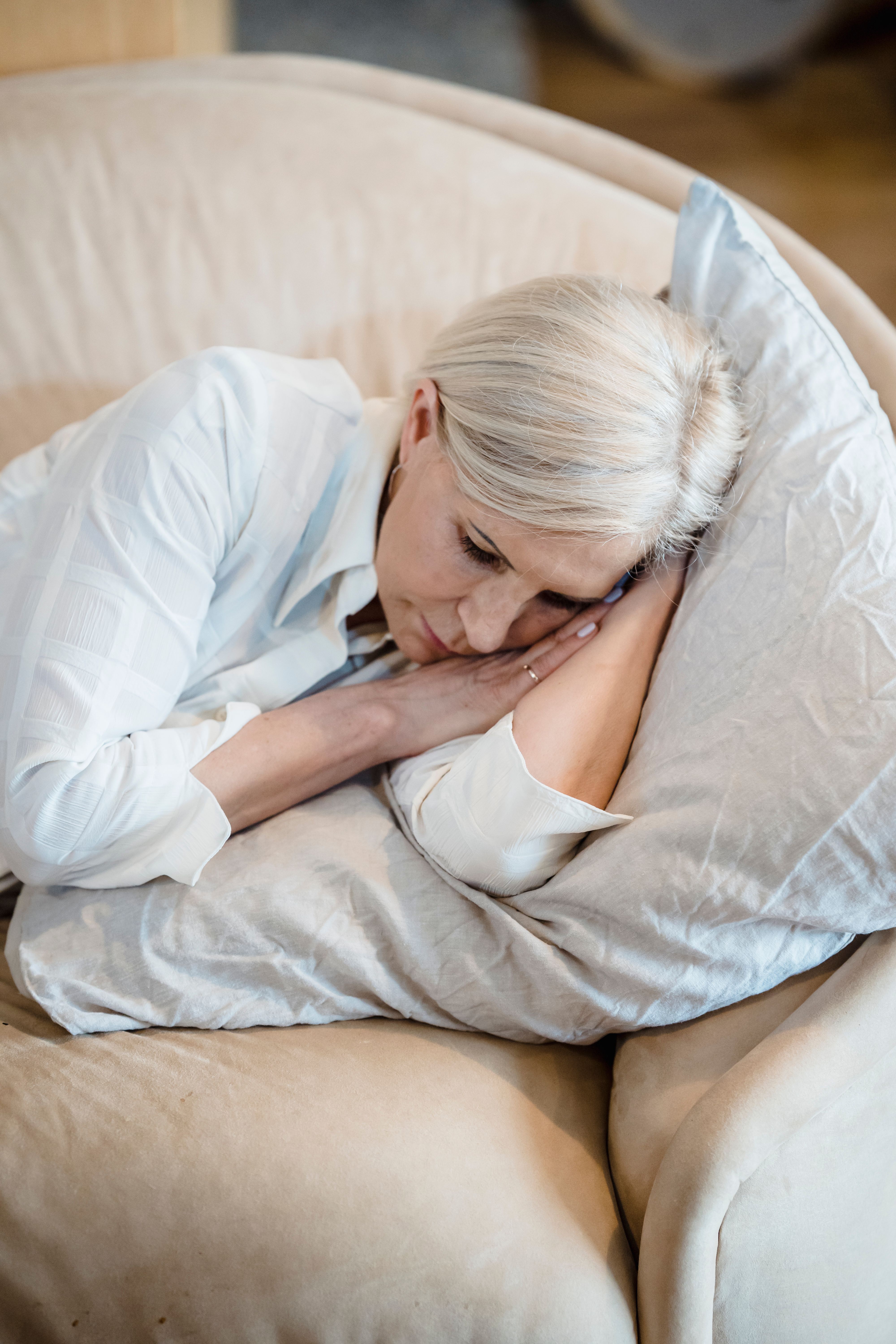Kvinne hviler p&aring; sofa med pute