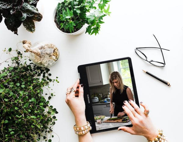Hands holding ipad with image of Megan chopping food on screen