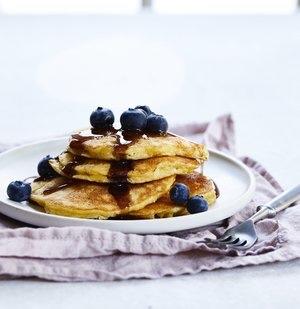 gluten free pancakes with blueberries on top and maple syrup stacked on a plate