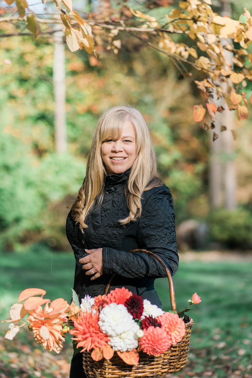 woman smiling holding a basket of dahlia flowers in the fall
