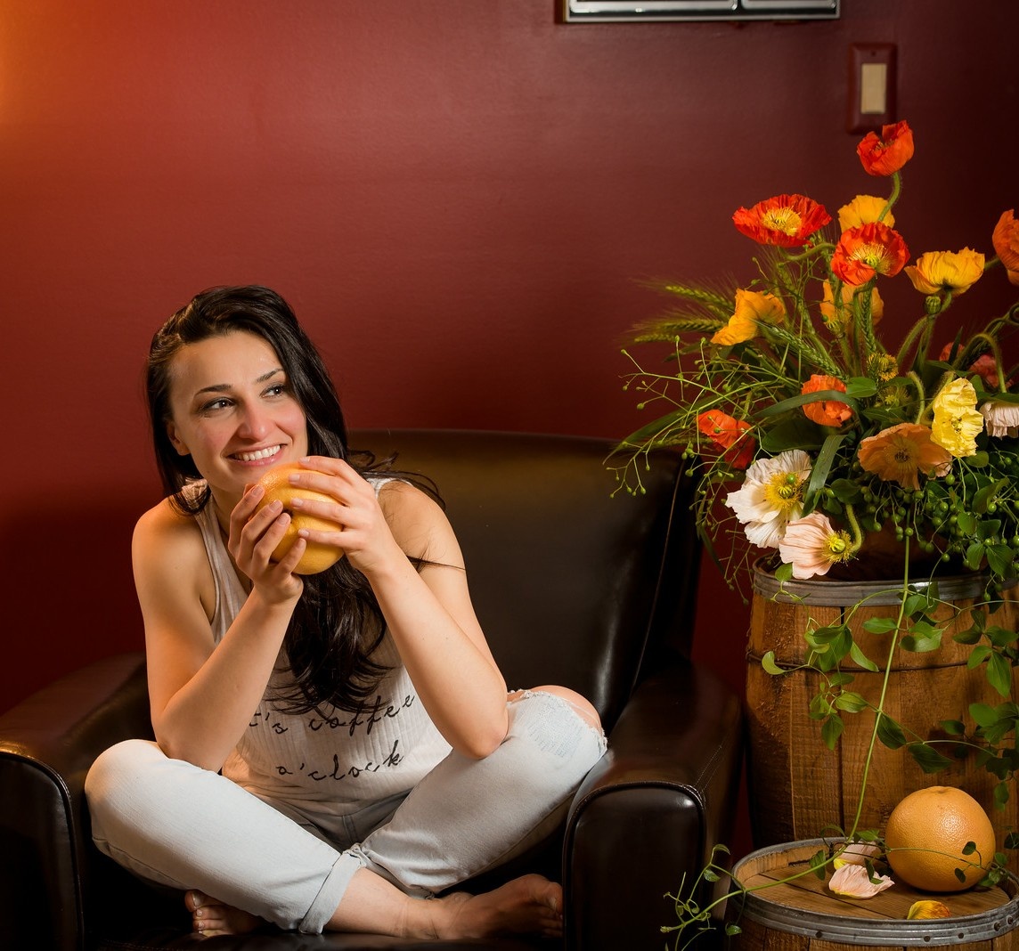 Girl seating holding a grapefruit next to orange yellow and red poppy flowers Anahit Viva La Flora Live Podcast host